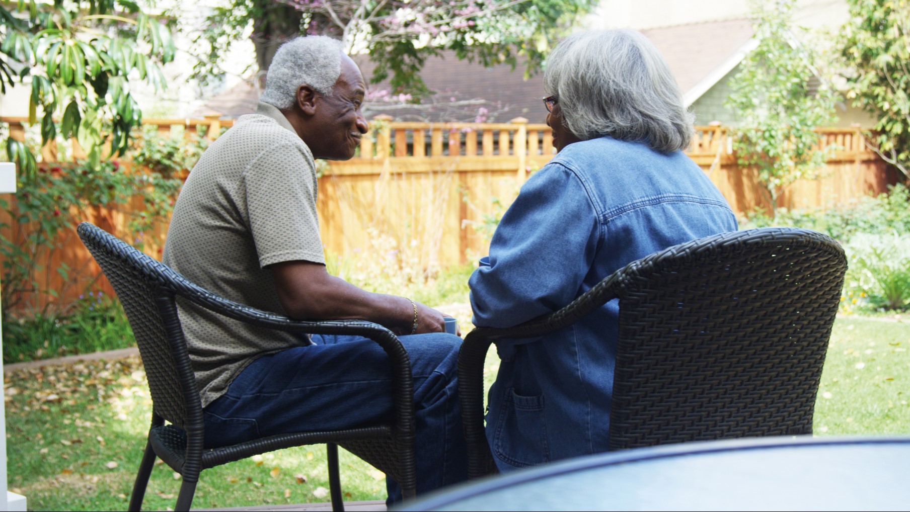 Older couple sat talking around a table in a sunny garden