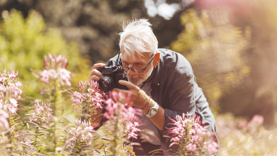 Older man taking pictures of pink flowers in a park, representing spending time in nature and focusing on hobbies